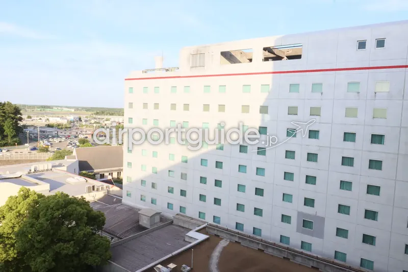 ホテル客室の窓から見た同ホテルの建物外観。白い外壁に赤いラインと緑がかった小窓が並ぶ大きな棟。