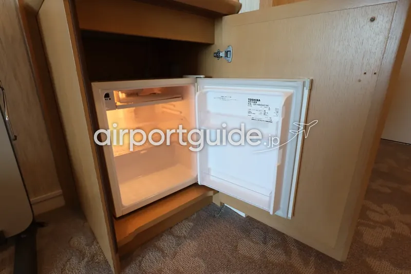 ホテル客室の木製キャビネットに収まる小型冷蔵庫（中は空）。扉を開けた状態のカット。