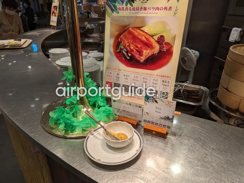 ライブキッチン付近。豚バラ肉の角煮の説明パネルと辛子の薬味、竹せいろが並び、奥にスタッフがいる。