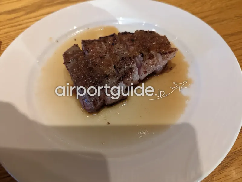 白い丸皿に盛られた牛サーロインステーキ。ソースに浸った一切れを寄りで撮影。