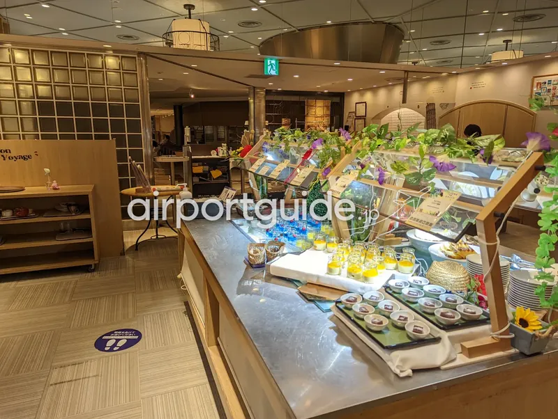 店内。デザートや前菜のショーケース付きカウンターが続き、奥に非常口サインと入口。