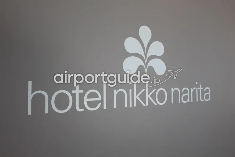 ホテルのロゴサイン。グレーの壁に花弁のシンボルマークと「hotel nikko narita」の文字。