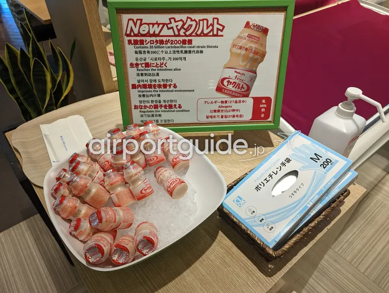 ホテル朝食会場のヤクルトのコーナー。氷の上にヤクルトが並び、多言語の説明POPとポリ手袋・消毒液が置かれる。