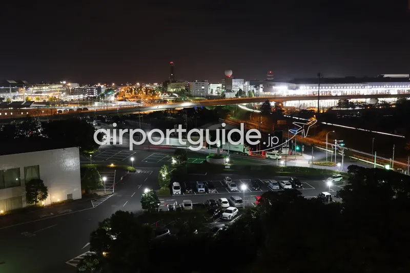 ホテルから望む成田空港周辺の夜景。奥にライトアップされたターミナルと高架道路、手前に街灯の点る駐車場。