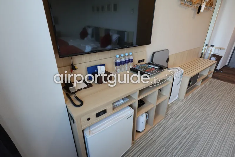 空港近くのホテル客室のテレビボード備品。冷蔵庫・ケトル・金庫・水が並ぶ。