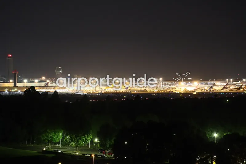 夜の成田空港全景。管制塔とターミナル、駐機する航空機を遠景で捉える。