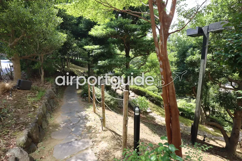 ホテル敷地内の庭園の遊歩道。石畳の小道と木製ロープ柵、緑の木立。