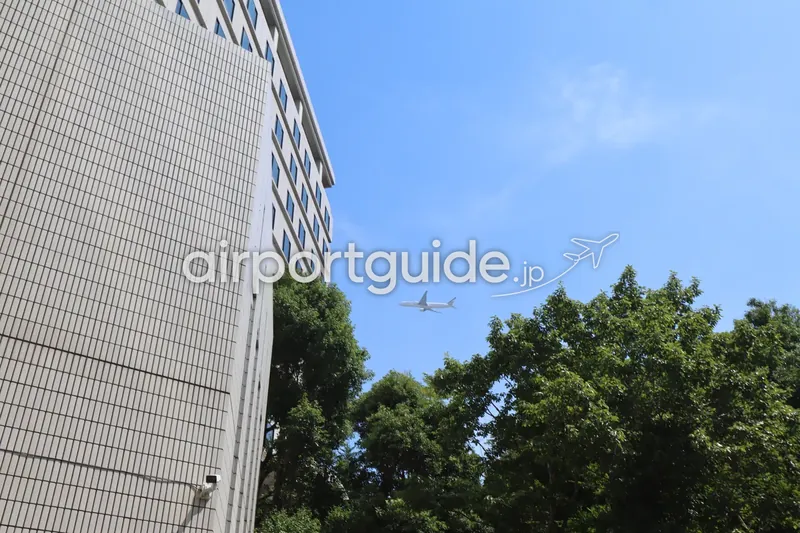ホテル上空を飛ぶ旅客機。成田空港へ向かう機体を地上から見上げた構図。