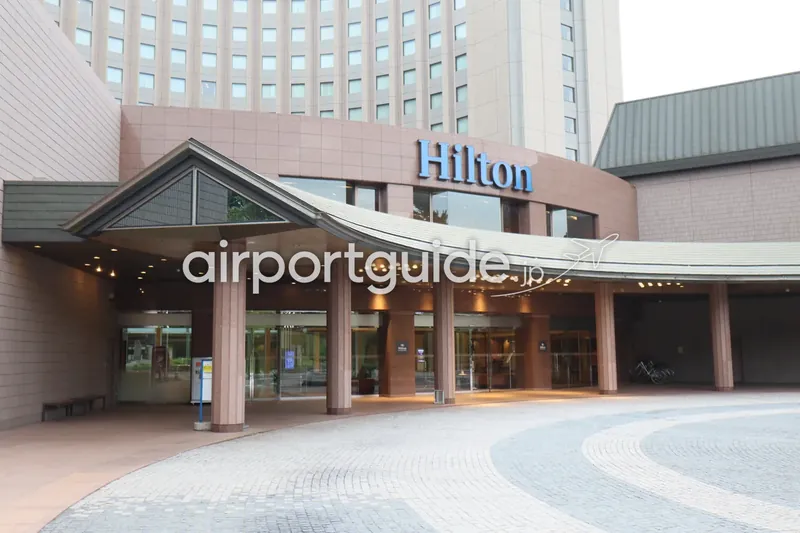 ヒルトン成田の玄関ポーチ（車寄せ）。湾曲した屋根と青い「Hilton」ロゴ、自動ドアの入口。