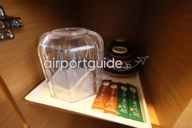 ホテル客室のお茶セットのクローズアップ。ガラスジャグ、縞模様の湯呑み、緑茶・焙じ茶のティーバッグ。