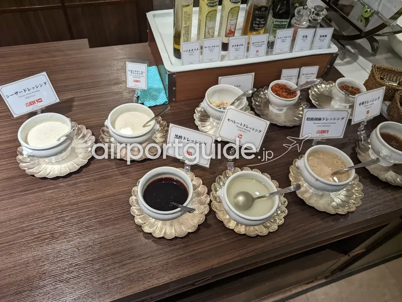 ドレッシングコーナー。貝型の銀皿に各種ドレッシングが並び、奥にオイルのボトルが立つ。