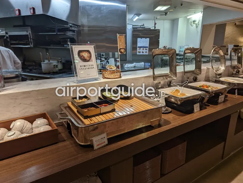 アートホテル成田の朝食レストランのビュッフェ台。ガラス越しの厨房を背に、保温チェーフィングが一列に並ぶ。