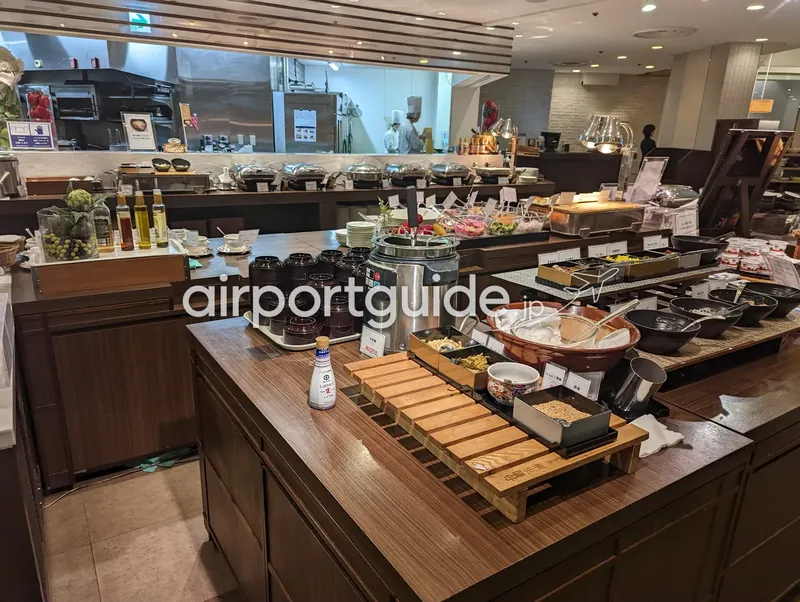 アートホテル成田の朝食レストラン全景。ガラス張りのオープンキッチンを背に、島型のビュッフェ台が広がる。