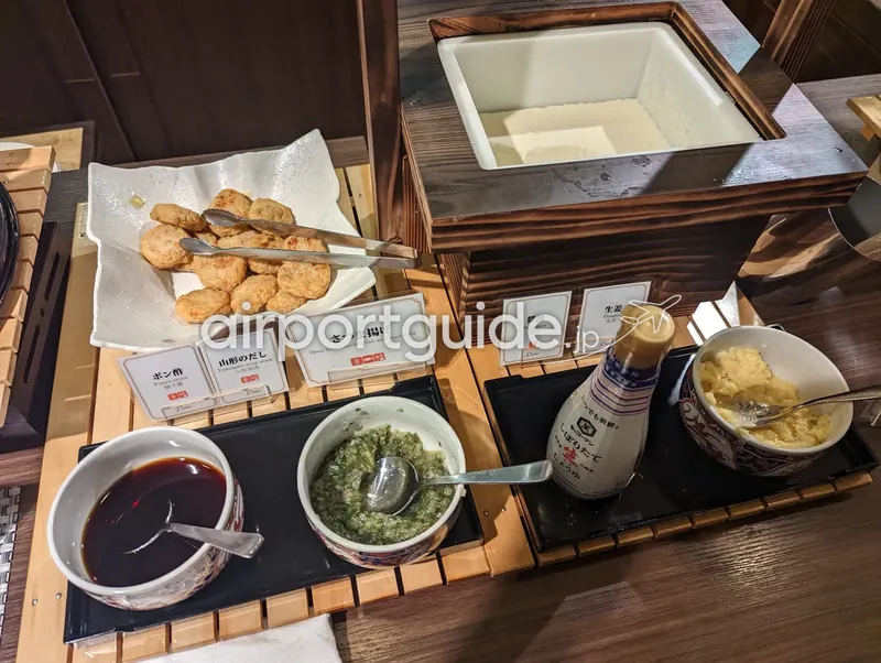 ホテル和朝食ビュッフェの豆腐・さつま揚げコーナーを俯瞰。木枠の器の豆腐と揚げ物、ポン酢・だし・醤油・生姜の薬味。