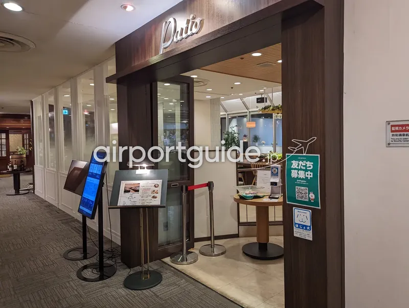 アートホテル成田の朝食レストラン『Patio』の入口を斜めから。筆記体ロゴの下にメニュースタンドとデジタルサイネージが並ぶ。