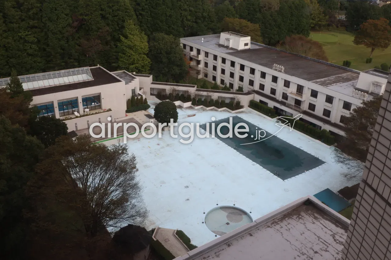 湯楽城の高層階から見下ろした屋外プールと客室棟。プールはシーズンオフでシートがかけられ、奥に林とゴルフ場の緑。