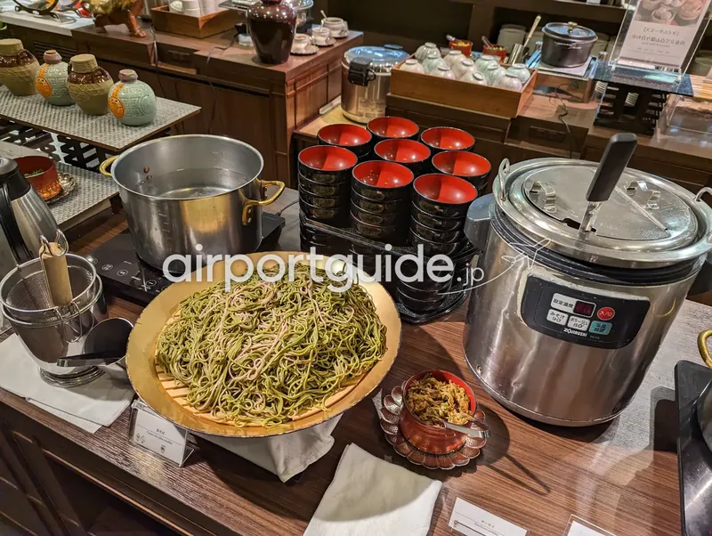 茶そばの麺コーナー。緑色の茶そばの大盛り、寸胴、黒椀、汁の保温ジャーが並ぶ。