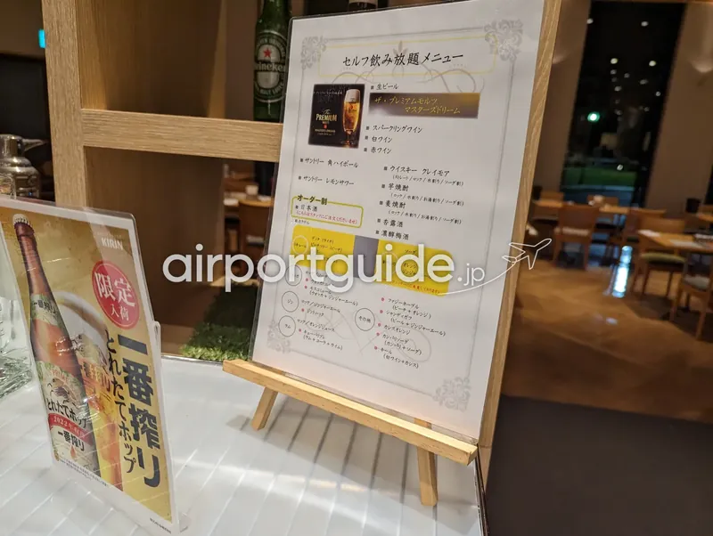 「セルフ飲み放題メニュー」の案内板がイーゼルに立てられている。奥にレストランの客席。