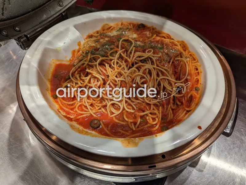 保温鍋の白い器に盛られたトマトソースのスパゲッティ（ケッパー入り）のアップ。