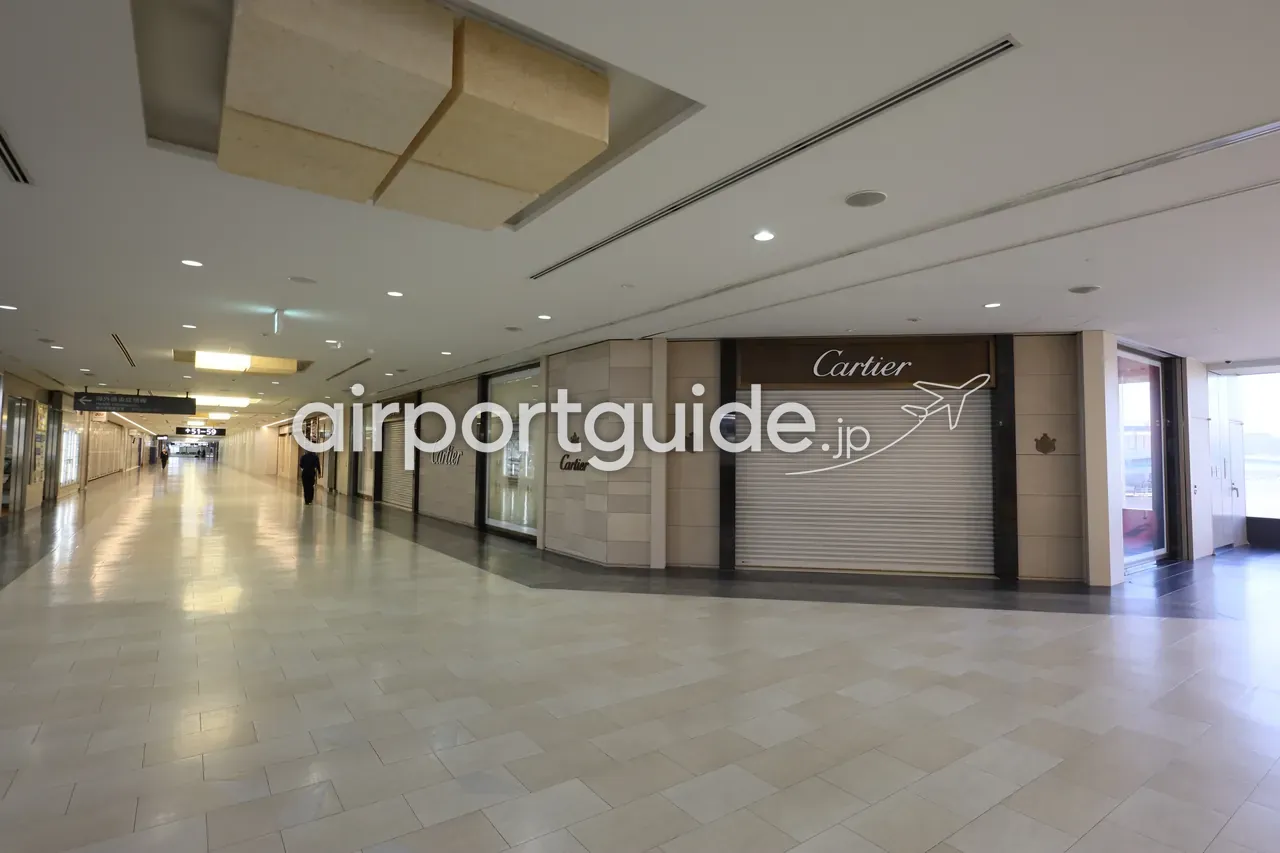 成田空港の制限エリア（海外免税店街）の通路。シャッターの下りた「Cartier」のブティックが並ぶ、静かな早朝の高級ブランド街。