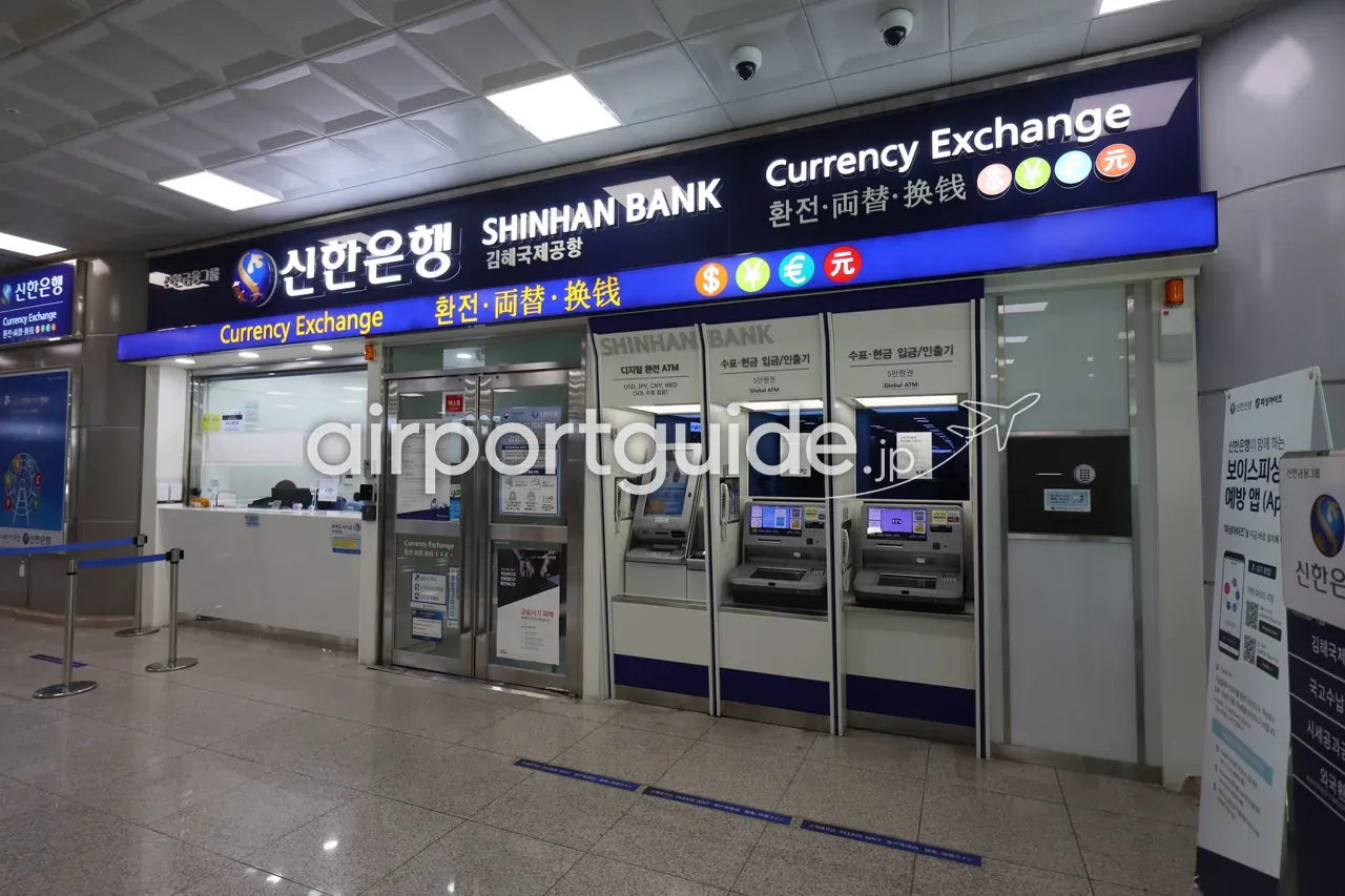金海空港・国際線到着エリアの新韓銀行（SHINHAN BANK）両替カウンター。「Currency Exchange 환전・両替・换钱」の看板と、右側に3台のGlobal ATM（両替ATM）が並ぶ。