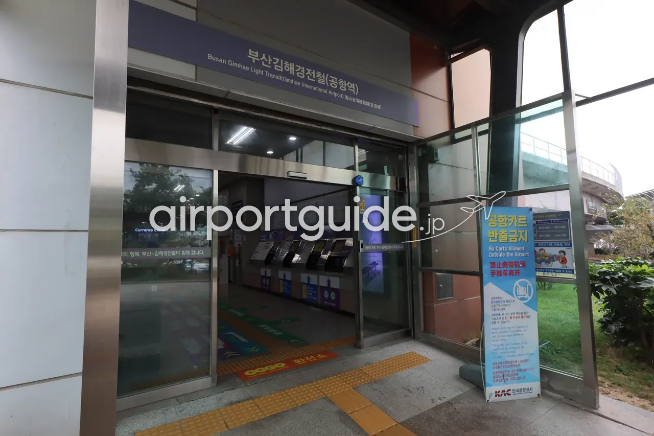 釜山金海軽電車『公港駅』の駅入口。ガラスの自動ドアの上に『부산김해경전철（Busan Gimhae Light Transit）공항역 Gimhae International Airport』の青い駅名サイン、内側に自動券売機、右手に韓国空港公社（KAC）の『공항카드 반출금지 / No Carts Allowed Outside the Airport』の注意幕。