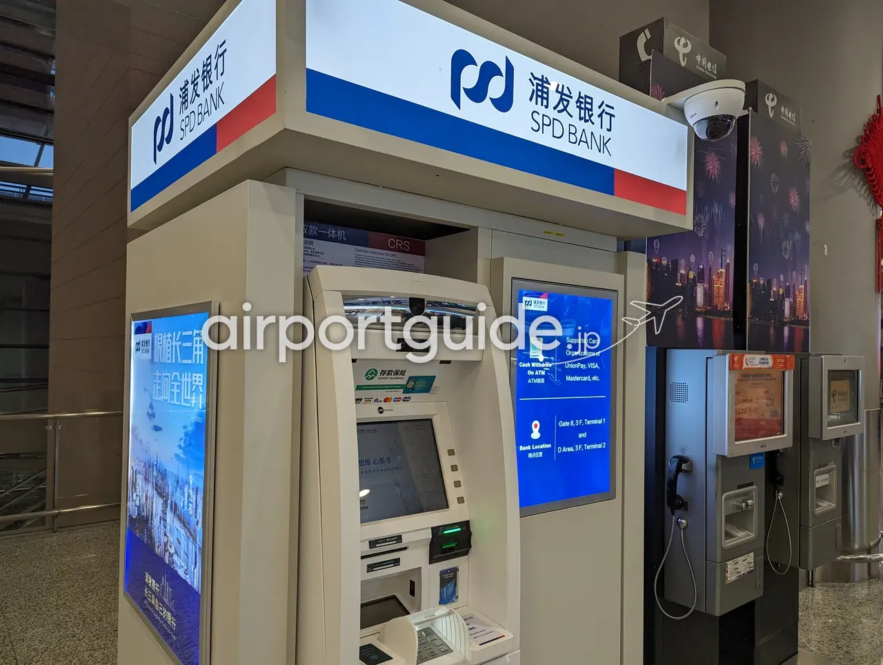 上海浦東空港のSPD BANK ATM（存取款一体機 CRS）。画面に『Cash Withdraw On ATM／Supported Card：UnionPay・VISA・Mastercard等』『Bank Location：Gate 8, 3F, Terminal 1／D Area, 3F, Terminal 2』、隣に中国電信の公衆電話。