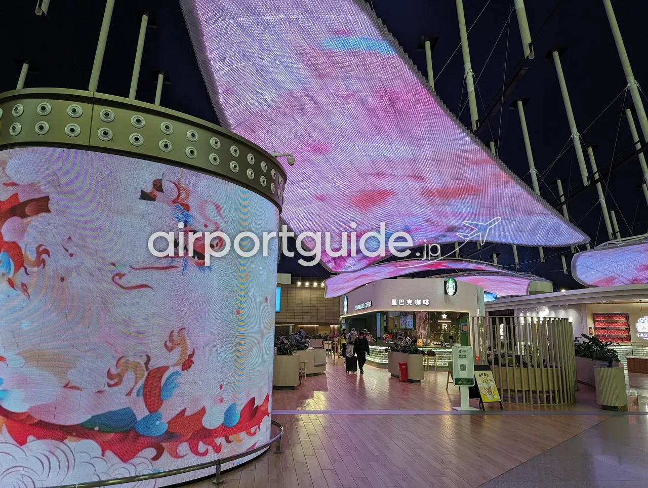 上海浦東空港の円柱形の巨大LEDメディアウォールに描かれた龍のデジタルアート。天井は波打つピンクのLED膜、奥にスターバックス(星巴克咖啡)。