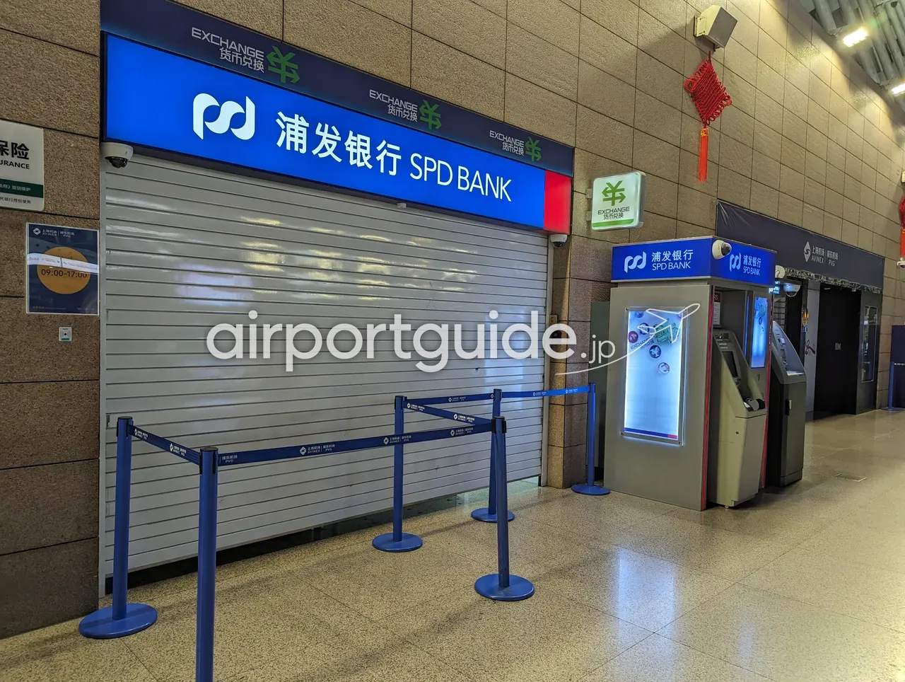 上海浦東空港・シャッターが下りた浦発銀行（SPD BANK）の両替窓口。青い「浦发银行 SPD BANK」看板と緑の「EXCHANGE 货币兑换」サイン、左側の柱に「09:00-17:00」の営業時間掲示。右隣にはSPD BANKの自動両替機とATMが並び、そちらは使える。