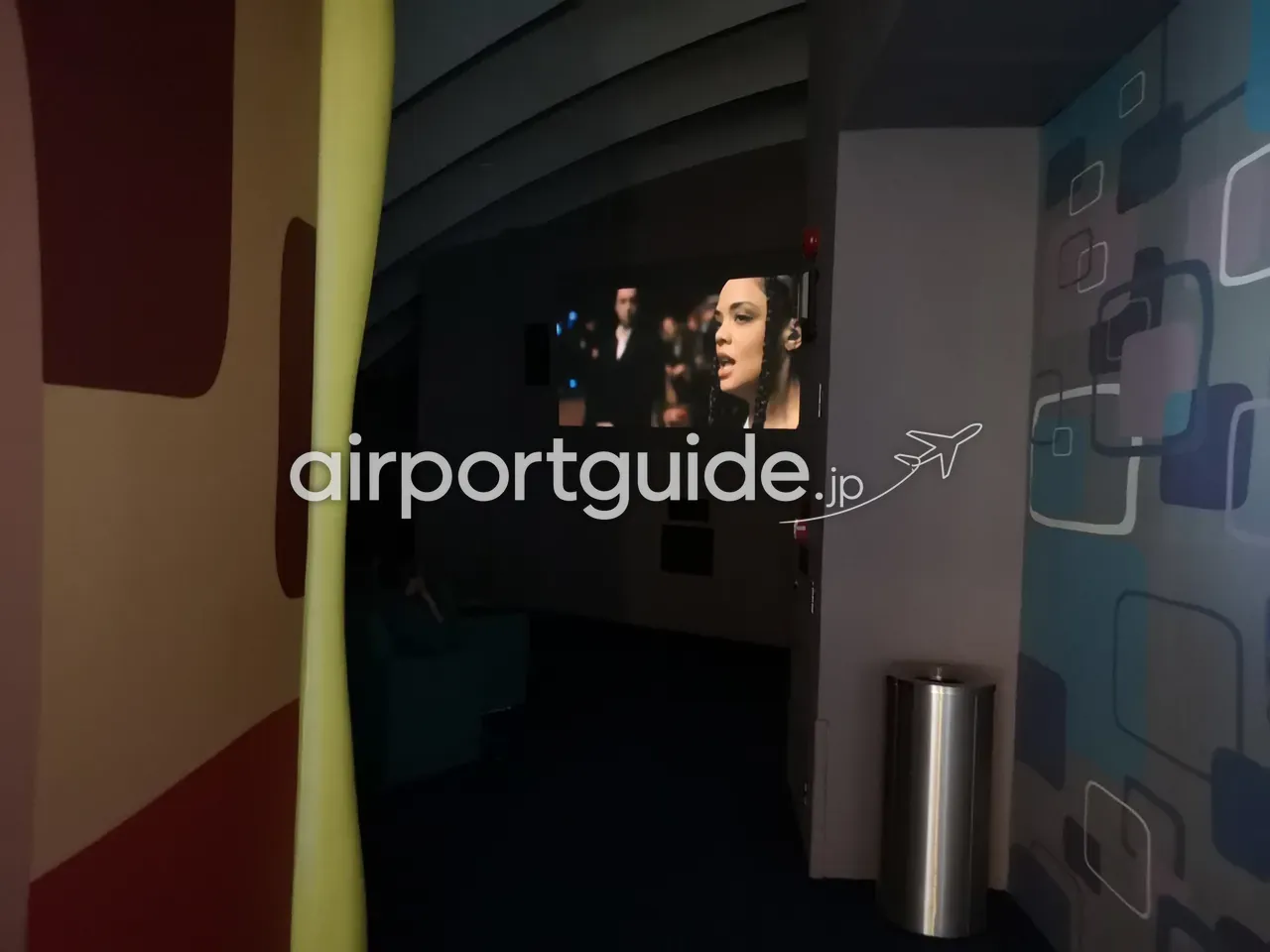 チャンギ空港の無料ムービーシアター／エンタメラウンジ。暗い室内でスクリーンに映画が映り、手前にソファ席。