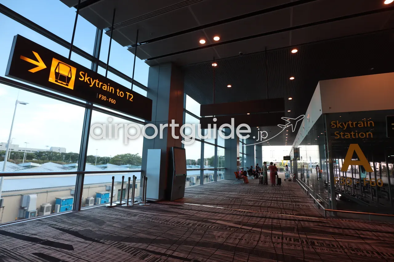 チャンギ空港のスカイトレイン乗り場。黄色い「Skytrain to T2」の吊りサインと、ガラス壁に大きく「Skytrain Station A」の表示。