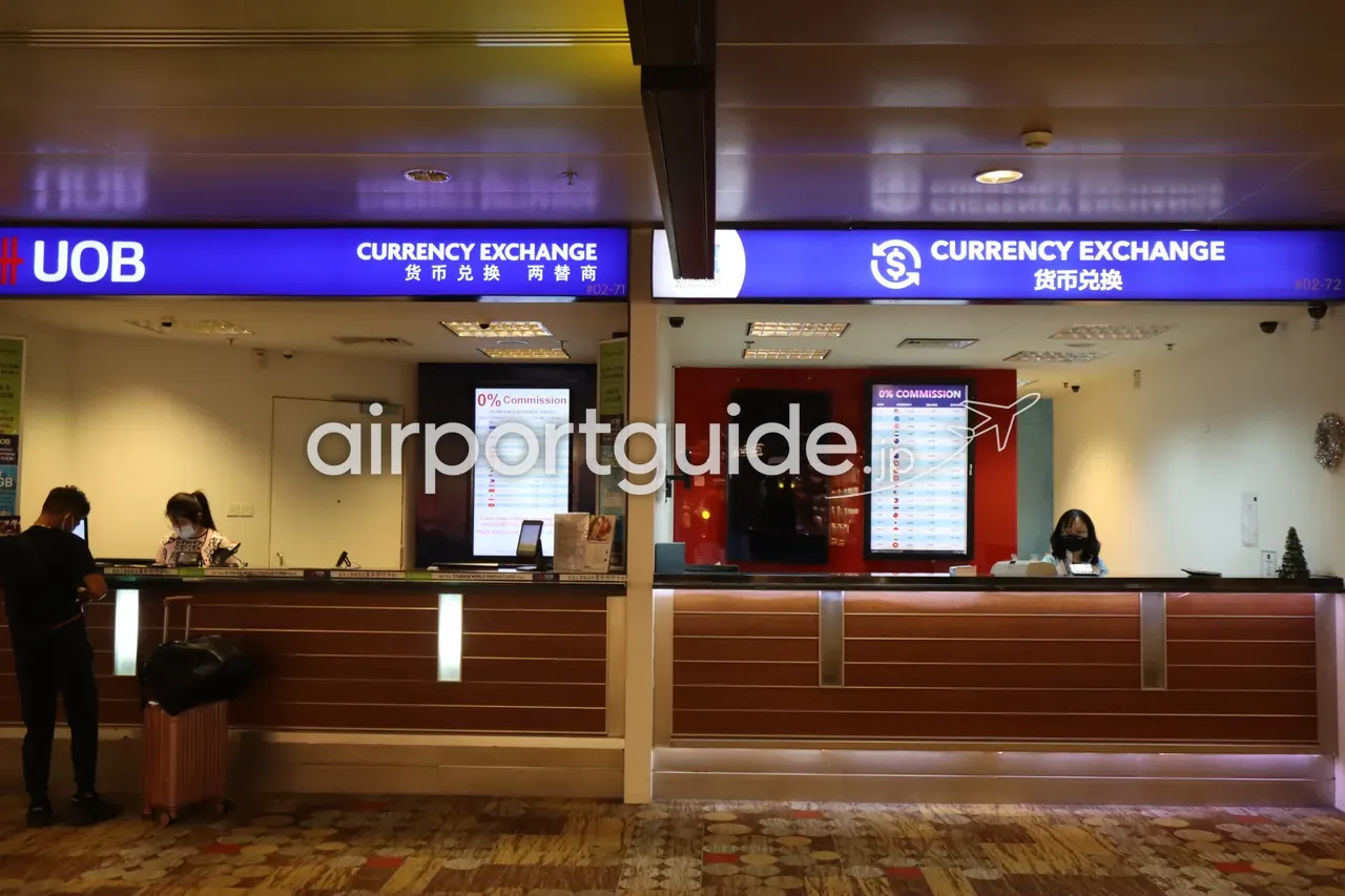 チャンギ空港の両替カウンター。左が「UOB Currency Exchange」、右が「Currency Exchange」で、いずれも「0% Commission」の外貨レート表を掲示。窓口で手続きする旅行者。