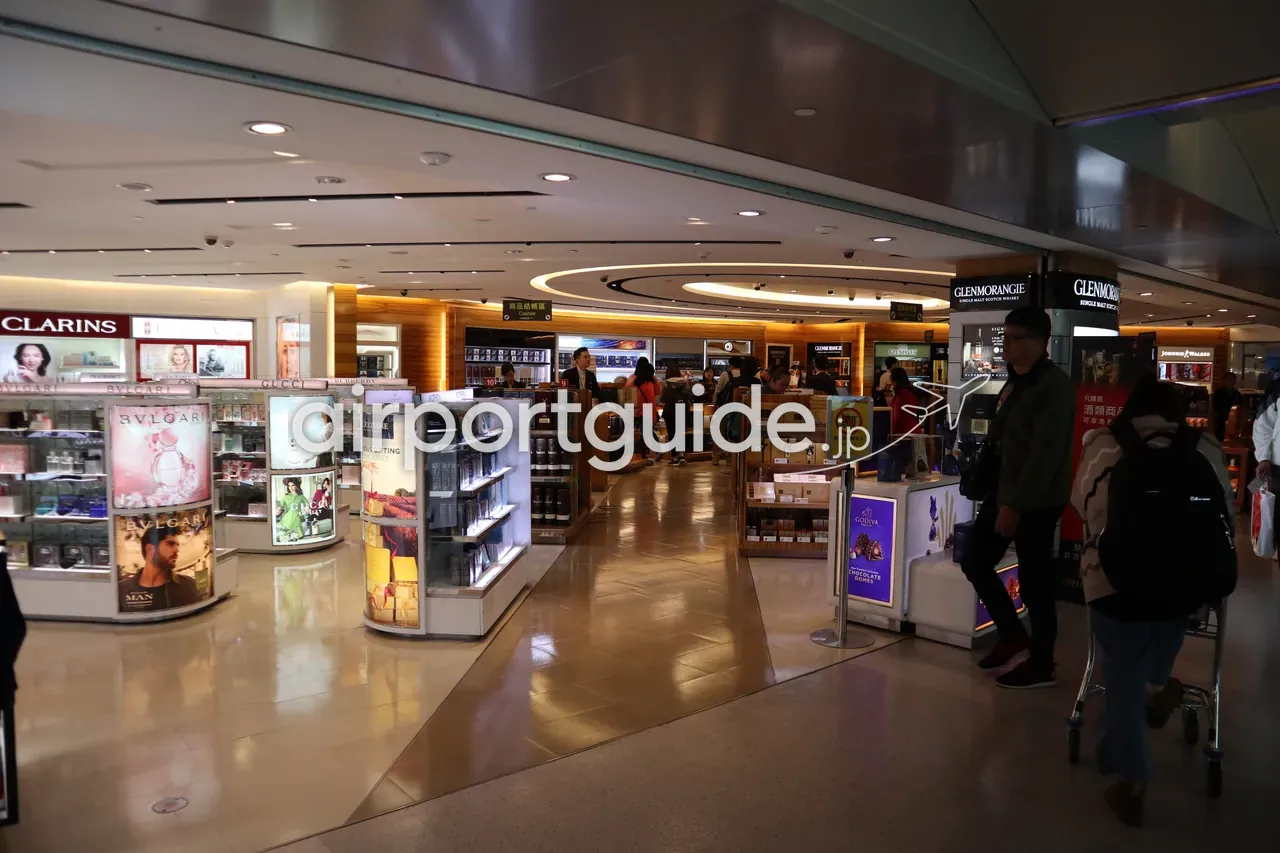 桃園空港の免税ショッピングエリア。CLARINS・BVLGARI・GUCCIなどの化粧品・香水コーナーと、Glenmorangie・Johnnie Walkerなどの洋酒コーナーが並び、買い物客が歩く。