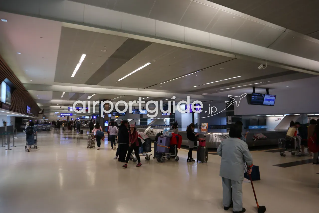 桃園空港の手荷物受取エリア。「2」の番号がついたターンテーブルとフライト案内モニターの下、カートを押す到着客と清掃スタッフ。