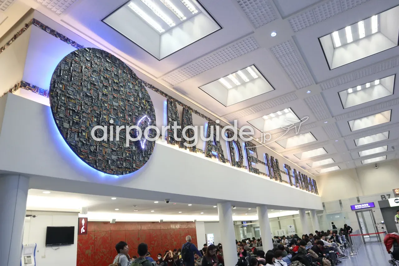 桃園空港の搭乗待合にあるアート「MADE IN TAIWAN」。電子基板でつくった円形のディスクと、基板を組んだ立体文字が青くライトアップされ、下に待合席の旅客。