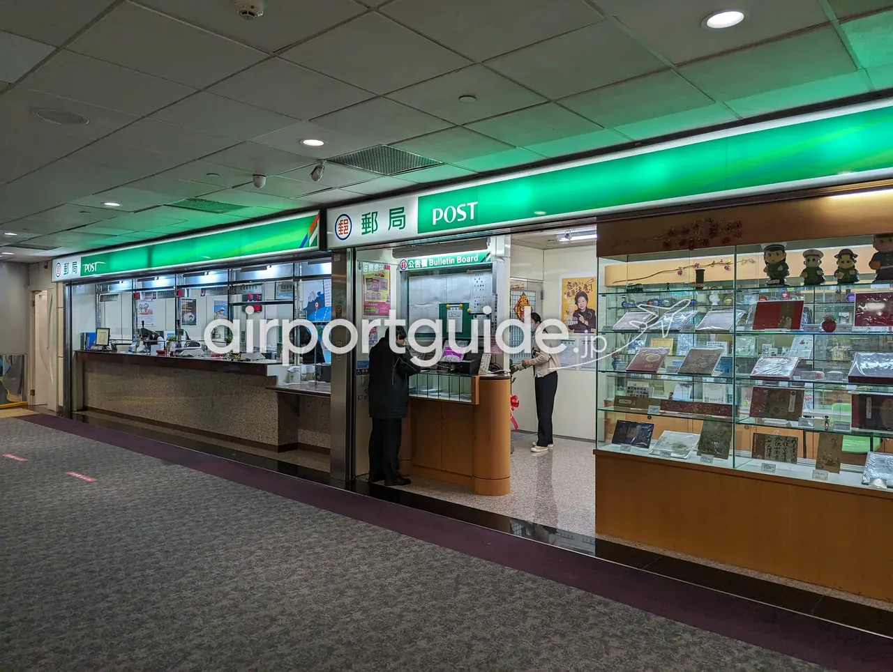 桃園空港内の郵便局「郵局 POST（中華郵政）」の緑の窓口。カウンターで手続きする利用客と、記念切手や土産の陳列ケース。