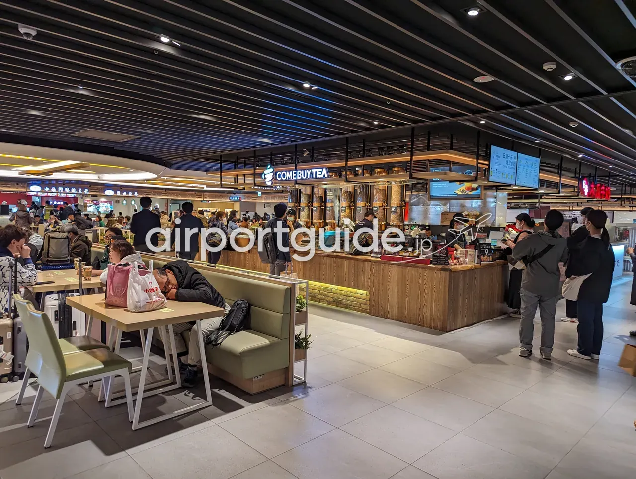 桃園空港のフードコートにあるタピオカティー店「COMEBUYTEA」。木目のカウンターに客が並び、手前のテーブル席で休む旅客。