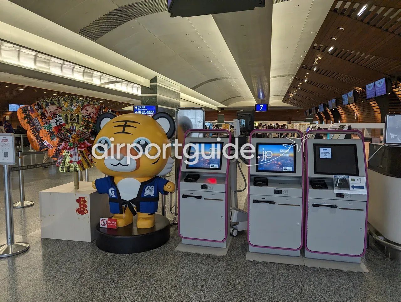 桃園空港のセルフチェックイン機が3台並ぶ一角。ピンク色の筐体にSITAのロゴ、脇にお祝いの花輪とマスコット像、奥に有人カウンター（7番）とゲート案内。