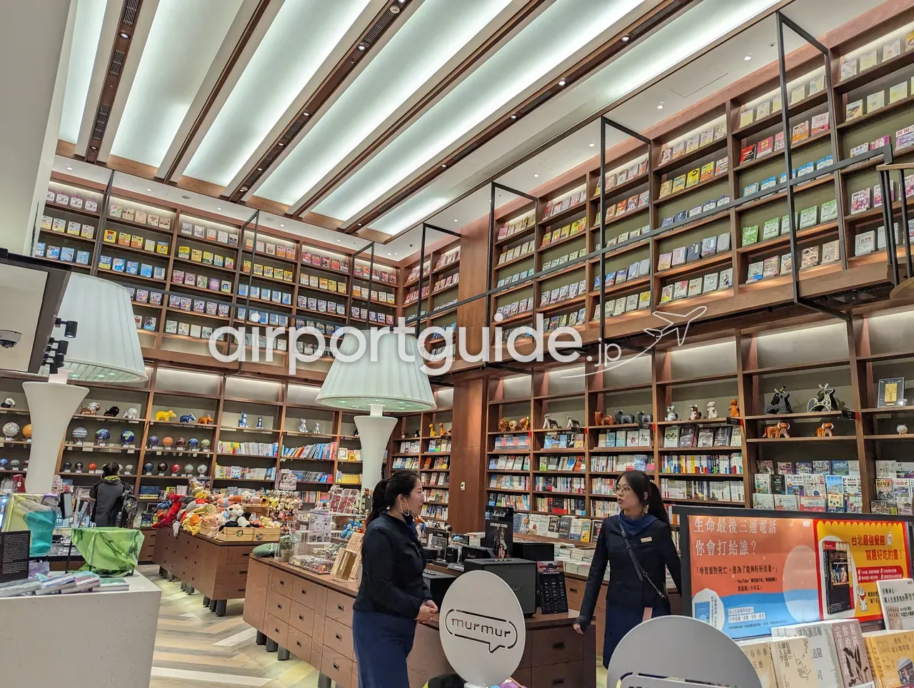 桃園空港内の書店。天井まで届く木製の高い本棚に多数の書籍が並び、手前に雑貨や玩具の陳列台。スタッフ2名が接客する。