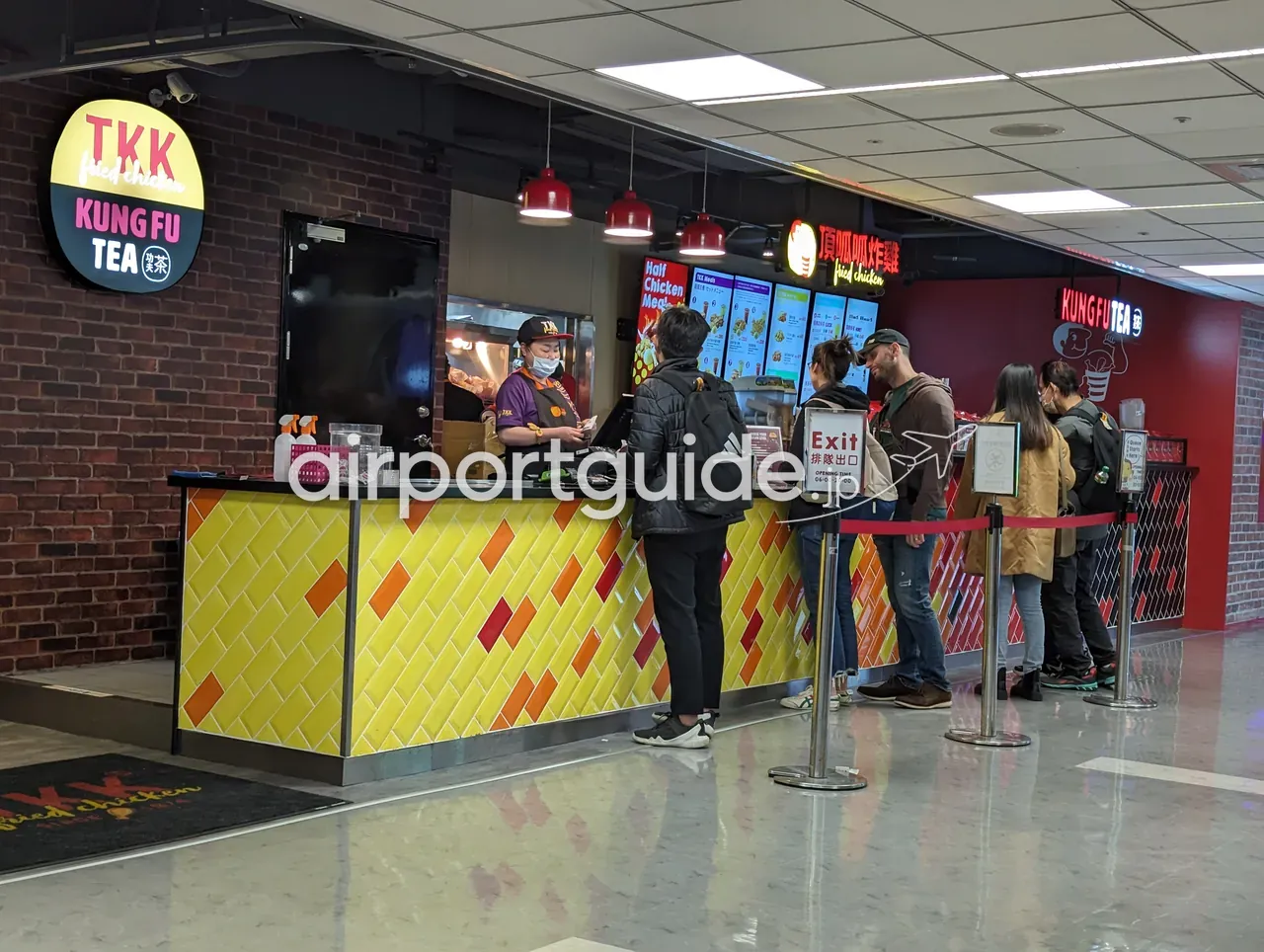 桃園空港の「TKK Fried Chicken／KUNG FU TEA（頂呱呱炸雞・功夫茶）」のカウンター。黄色いタイルのカウンター前にメニュー板と行列、スタッフが調理・接客する。