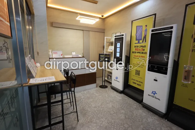 セルフチェックイン機（SELF CHECK IN/OUT SYSTEM）。「Check In Here」の案内と問い合わせ先 1599-6621。